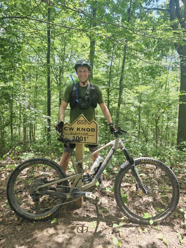 Person with a mountain bike poising at a sign in a forest